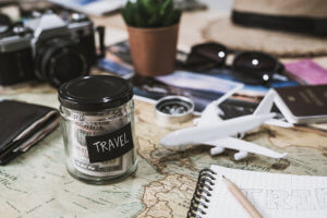 Vacation savings in a jar with map, notebook, and sunglasses on table